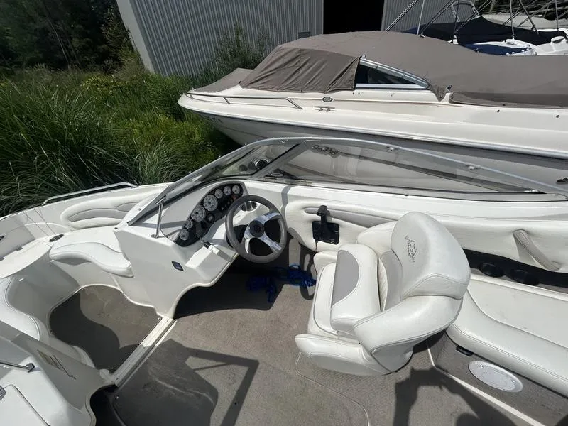 Slide: The Image of 2007 Stingray 210LR boat interior with white seating and dashboard, parked near greenery. - 5