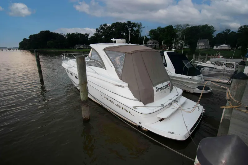Slide: The Image of 2003 Regal Commodore 4260 yacht docked at a marina, surrounded by calm water and trees. - 2