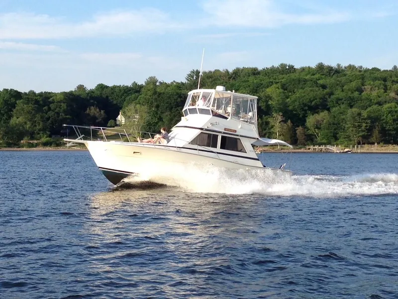 Slide: The Image of 1986 Viking 35 Convertible yacht cruising on a scenic lake with lush green forest backdrop. - 2