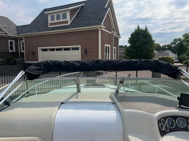 Slide: The Image of 2000 Crownline 242 CR boat with covered windshield, parked near a house. - 12