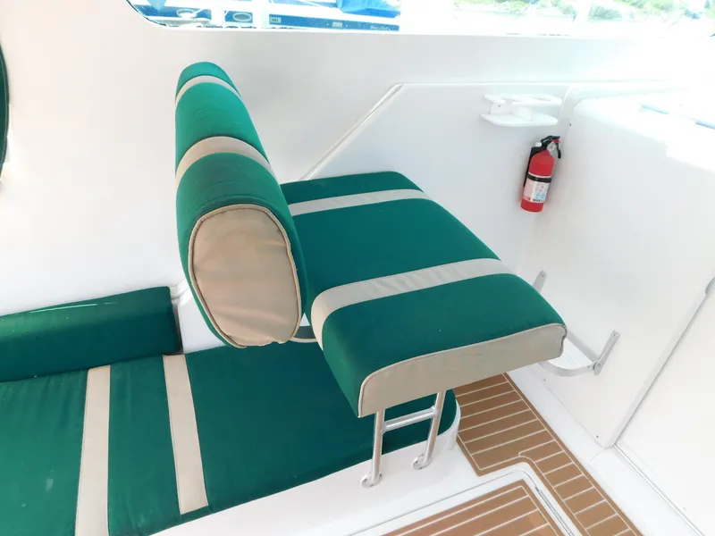 Slide: The Image of 1999 Mainship Pilot 30 interior with green and beige seating, fire extinguisher, and wooden flooring. - 30