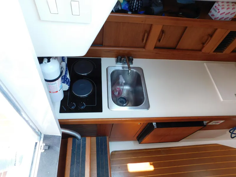Slide: The Image of 1999 Mainship Pilot 30 galley with stove, sink, and wooden cabinetry. - 36