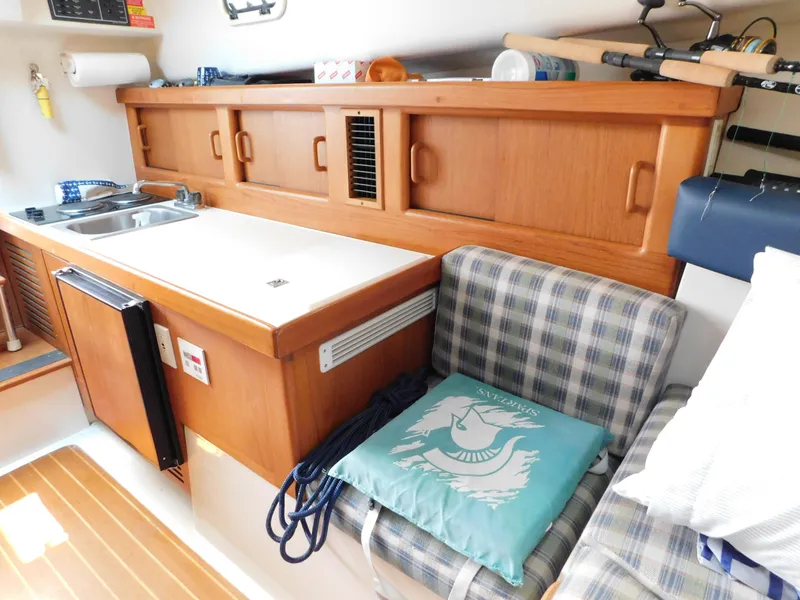 Slide: The Image of 1999 Mainship Pilot 30 interior with kitchenette, plaid seating, and nautical-themed cushion. - 43