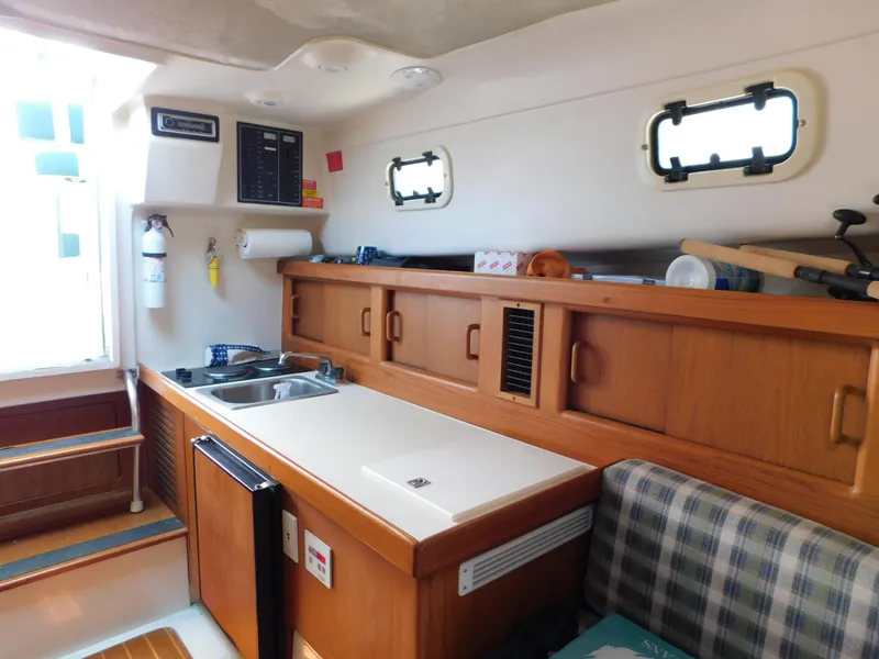 Slide: The Image of 1999 Mainship Pilot 30 interior with kitchenette, wooden cabinets, and seating area. - 44