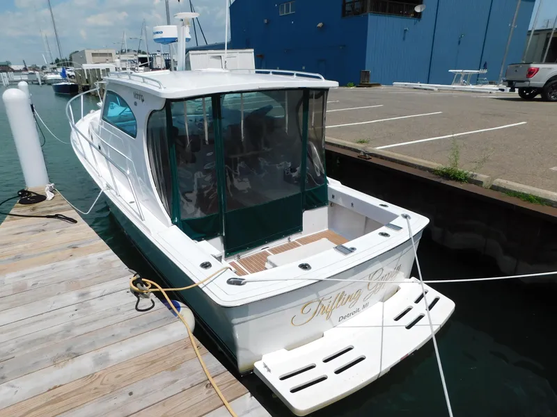 Slide: The Image of 1999 Mainship Pilot 30 docked at marina, featuring white hull and green canopy. - 6