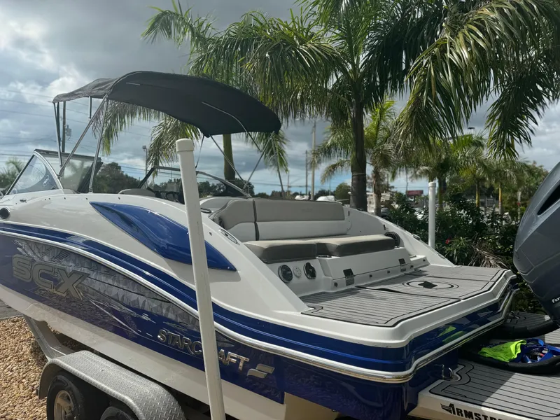 Slide: The Image of 2017 Starcraft 230 OB SCX EXT boat with canopy, parked near palm trees. - 11