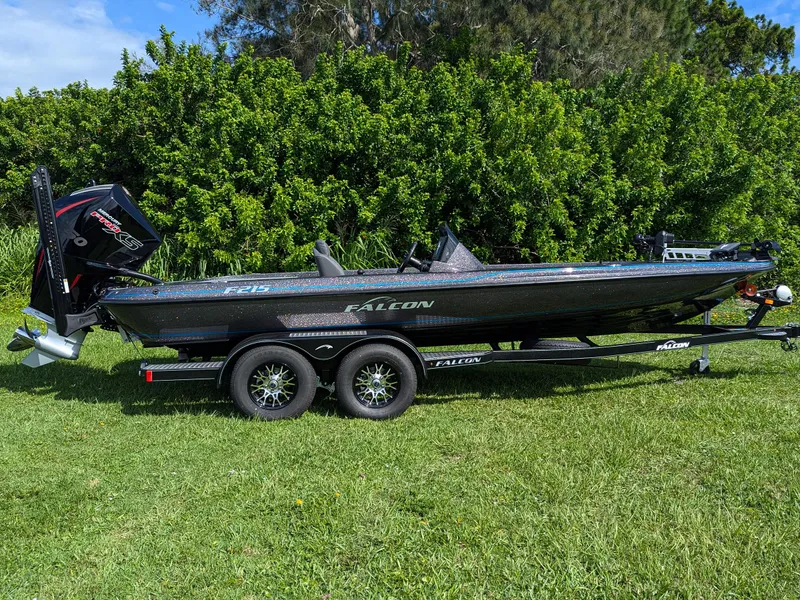 Slide: The Image of 2026 Falcon F215 boat on trailer, parked on grass with lush greenery background. - 2