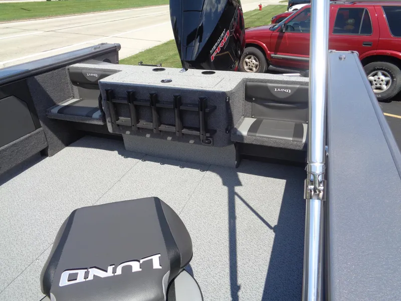 Slide: The Image of 2025 Lund 2075 Fisherman boat interior with seating and motor, parked near a red SUV. - 5