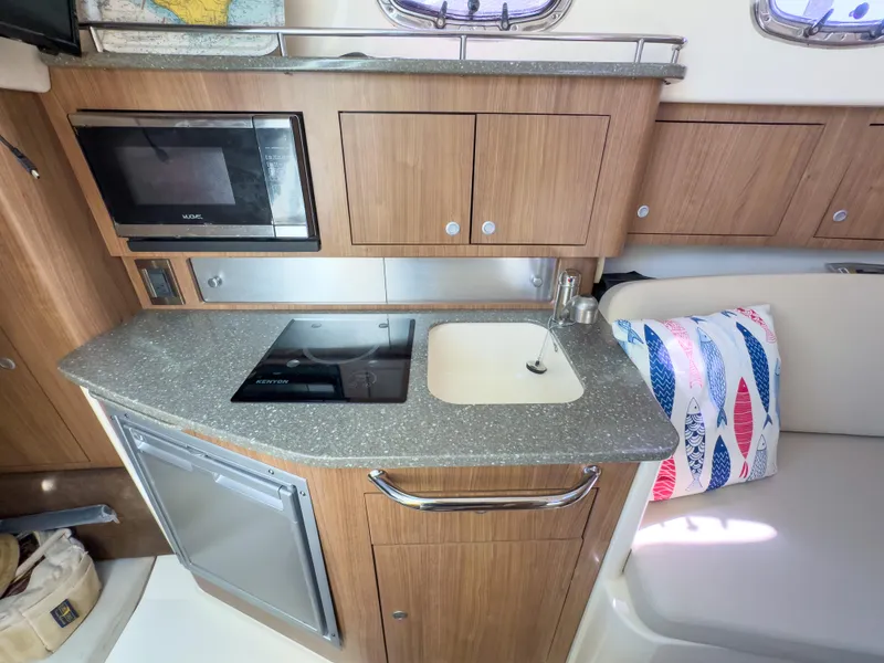 Slide: The Image of 2018 Boston Whaler 315 Conquest galley with microwave, stove, sink, and seating area. - 36