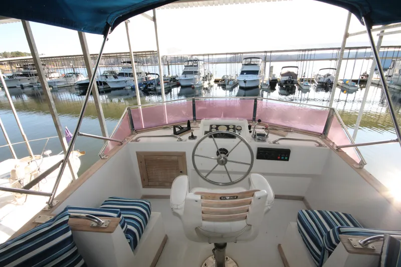 Slide: The Image of 1986 Senator 35 Sundeck Trawler helm with marina view, featuring striped seating and navigation controls. - 15