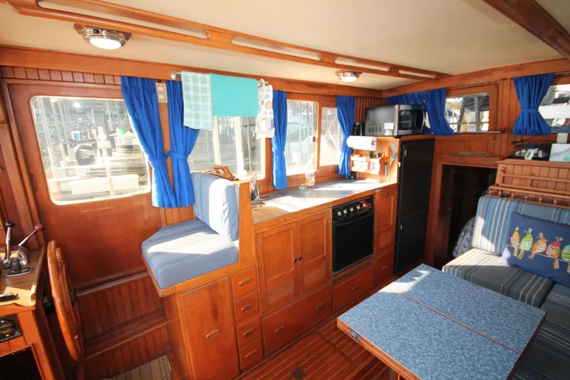 Slide: The Image of 1986 Senator 35 Sundeck Trawler interior with wood finish, blue curtains, and seating area. - 21