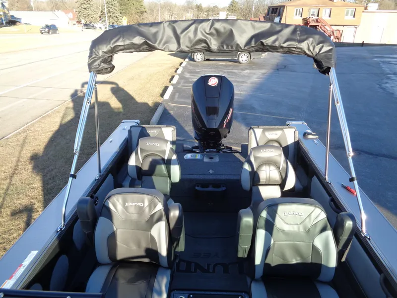 Slide: The Image of 2025 Lund 1875 Tyee boat interior with seating and motor, parked on pavement. - 17