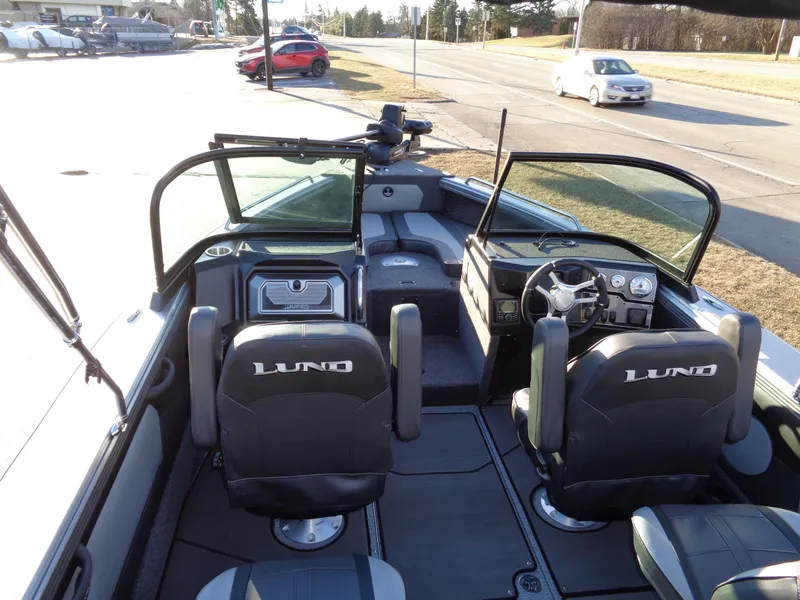 Slide: The Image of 2025 Lund 1875 Tyee boat interior with steering wheel and seating, parked near road. - 7
