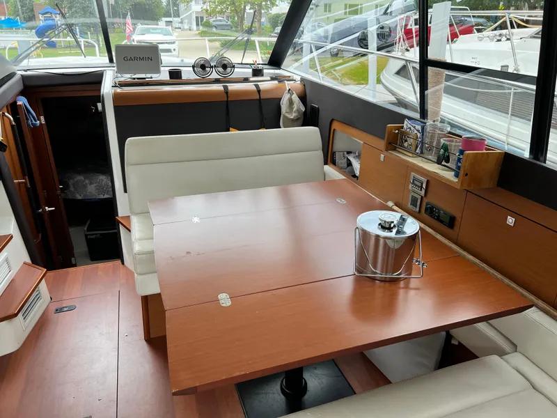 Slide: The Image of Interior of a 2017 Jeanneau NC11 boat with a wooden dining table and white seating. - 11