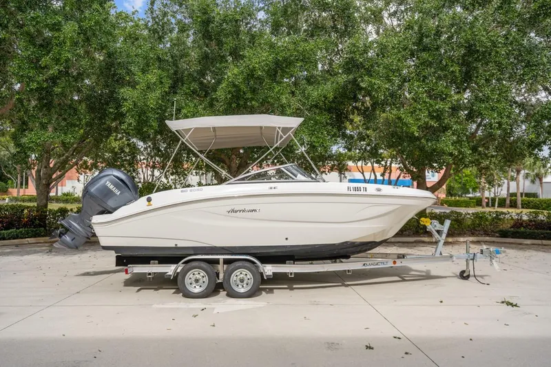Slide: The Image of 2025 Hurricane SunDeck 2050 OB boat on trailer, parked outdoors with trees in background. - 3