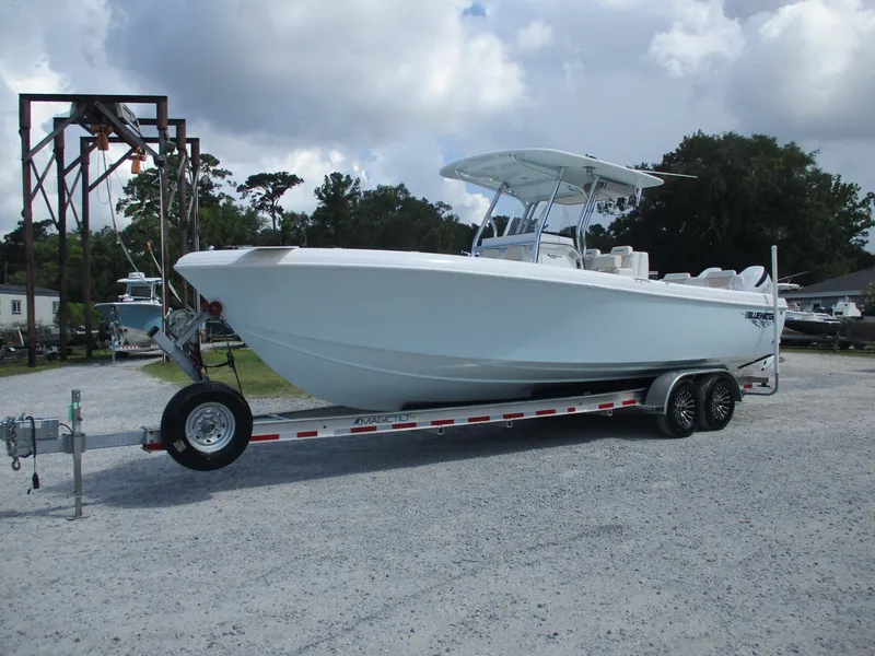 Slide: The Image of 2024 Bluewater 2850 boat on trailer, parked outdoors under cloudy sky. - 2