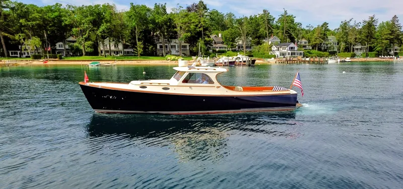 The Image of 2000 Hinckley Picnic Boat cruising on a serene lake with lush greenery and waterfront homes. - 0