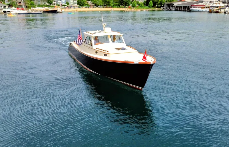 Slide: The Image of Hinckley Picnic Boat 2000 cruising on a serene lake near a bustling shoreline. - 15