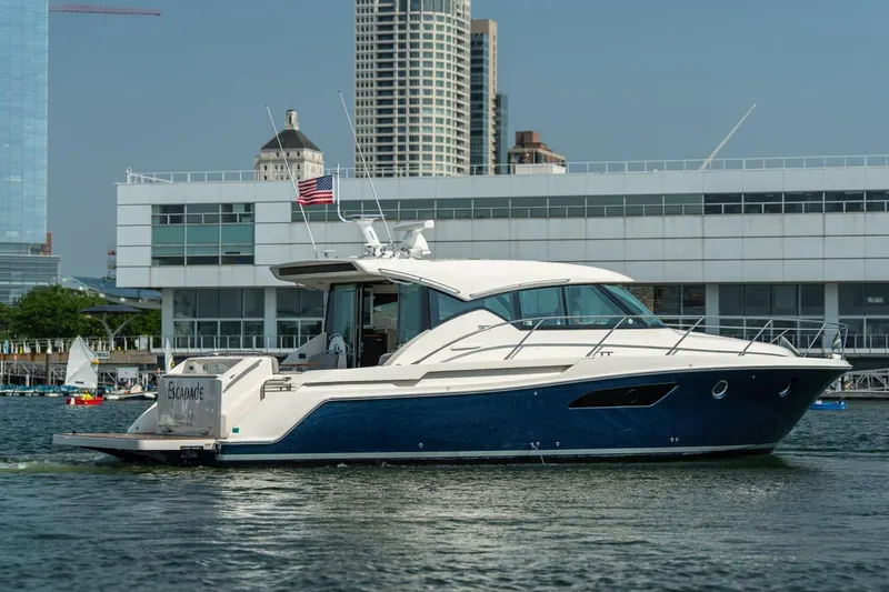 Slide: The Image of 2017 Tiara Yachts C44 Coupe cruising near modern waterfront buildings. - 11