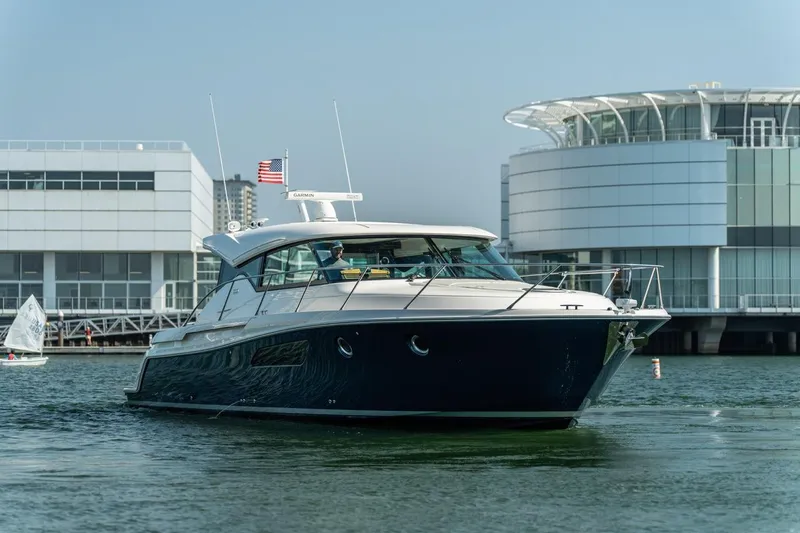 Slide: The Image of 2017 Tiara Yachts C44 Coupe cruising near modern waterfront buildings. - 14