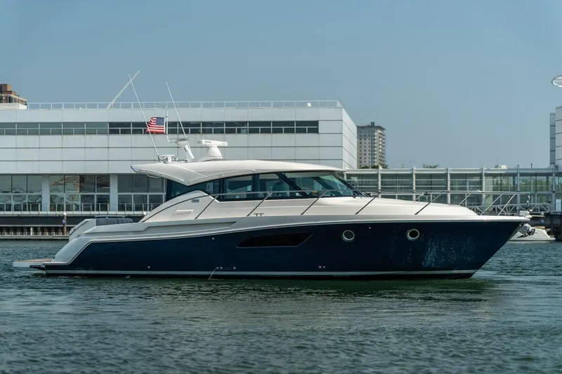 Slide: The Image of 2017 Tiara Yachts C44 Coupe in marina, sleek design, American flag, modern architecture backdrop. - 16