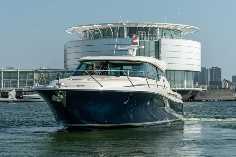 Slide: The Image of 2017 Tiara Yachts C44 Coupe cruising near modern waterfront architecture. - 2