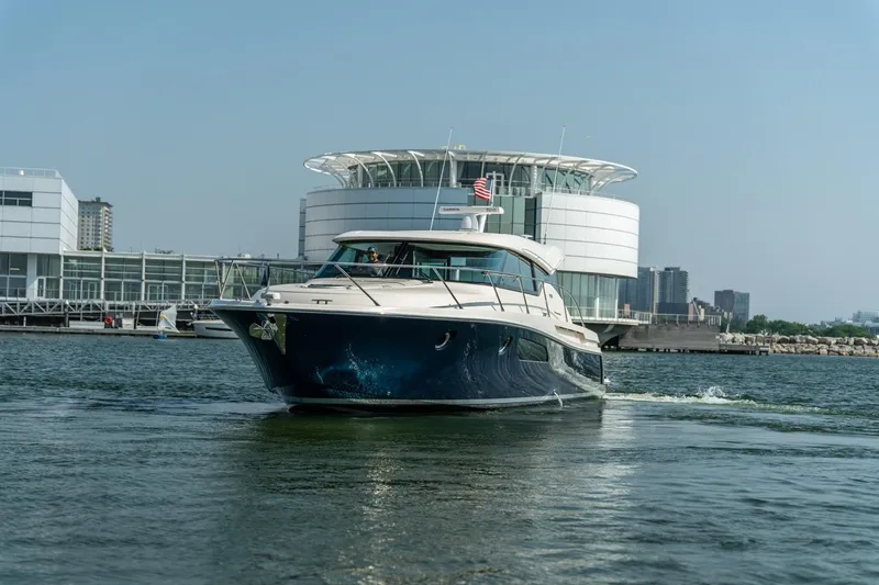 Slide: The Image of 2017 Tiara Yachts C44 Coupe cruising near modern waterfront architecture. - 30