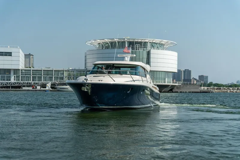 Slide: The Image of 2017 Tiara Yachts C44 Coupe cruising near modern waterfront architecture. - 31