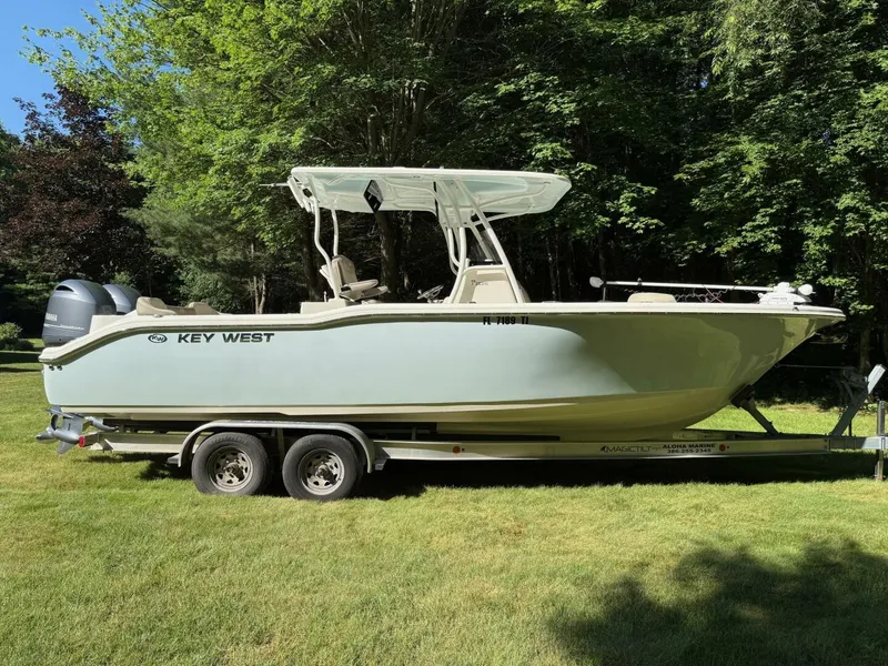 Slide: The Image of 2023 Key West 263 FS boat on trailer, parked on grass, surrounded by trees. - 2