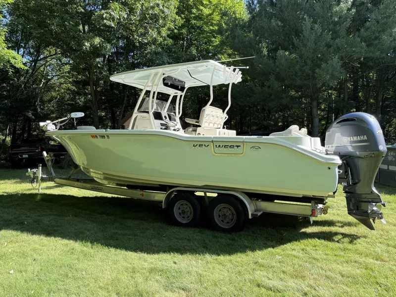 Slide: The Image of 2023 Key West 263 FS boat on trailer, parked on grass, surrounded by trees. - 7