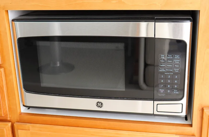 Slide: The Image of A built-in GE microwave oven with a stainless steel finish, set in wooden cabinetry. - 18
