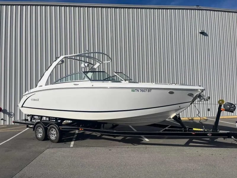 Slide: The Image of 2021 Cobalt R7 boat on trailer, parked outdoors against a corrugated metal wall. - 2