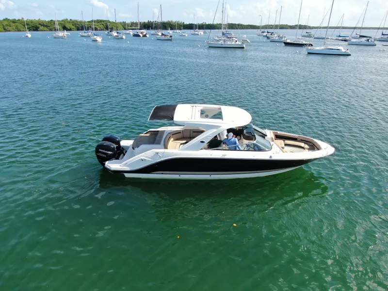 Slide: The Image of 2018 Sea Ray 310 SLX boat cruising on a calm, scenic bay with sailboats in the background. - 6