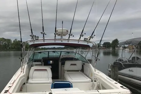 The Image of 1992 Sea Ray 310 Amberjack boat with fishing rods docked on a calm lake. - 0