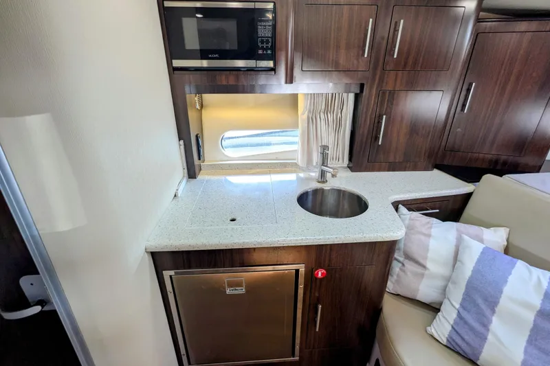 Slide: The Image of 2018 Regal 33 XO yacht interior kitchen with microwave, sink, and wooden cabinets. - 25