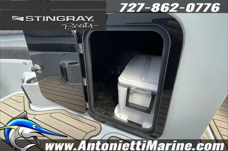 Slide: The Image of 2026 Stingray 23 OSX boat storage compartment with cooler, featuring marine flooring and branding. - 24