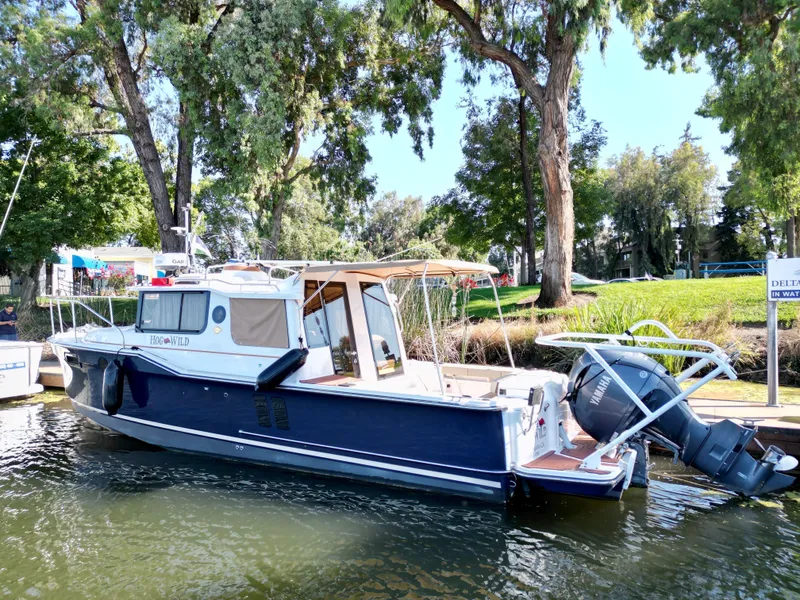Slide: The Image of 2023 Ranger Tugs R-27 boat docked by lush greenery, featuring a Yamaha outboard motor. - 12