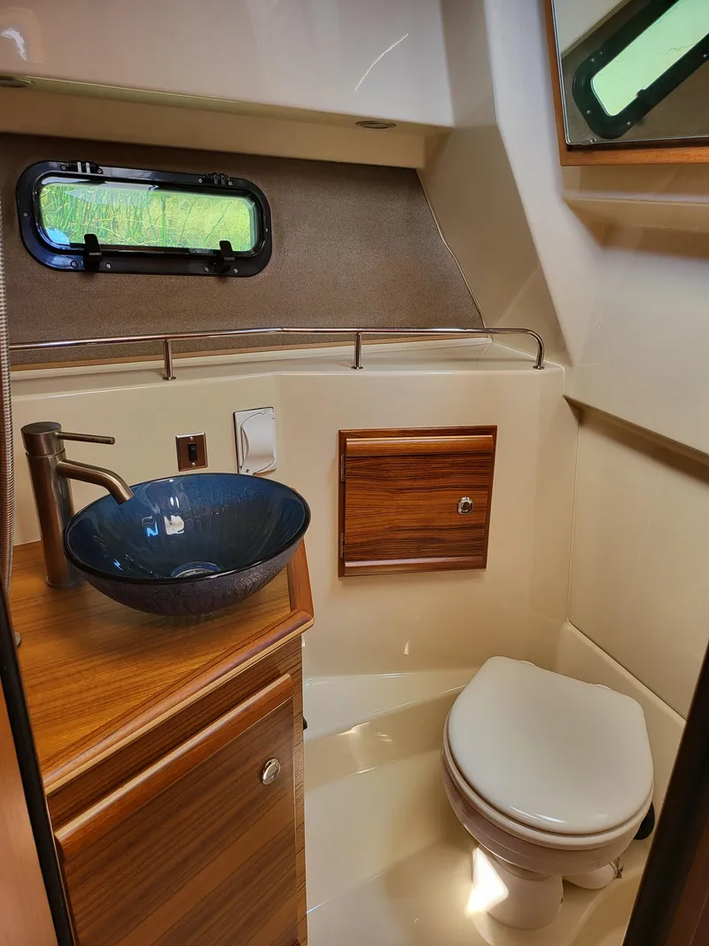 Slide: The Image of 2023 Ranger Tugs R-27 bathroom with modern sink, wooden cabinetry, and compact toilet. - 16