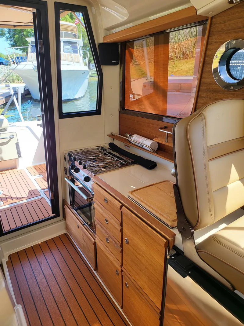 Slide: The Image of Interior of 2023 Ranger Tugs R-27, featuring a compact kitchen with stove and wooden cabinetry. - 19