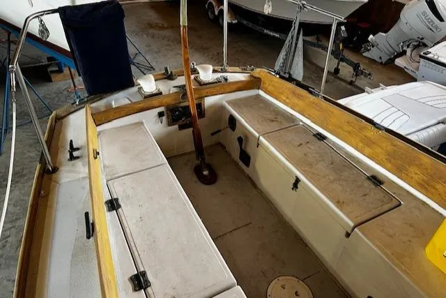 Slide: The Image of 1977 Cape Dory Sloop cockpit with wooden tiller and storage compartments in a marina setting. - 16