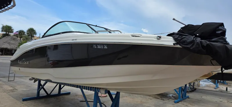 Slide: The Image of 2019 NauticStar 223DC Sport Deck boat on display, elevated on stands, with a sleek black and white design. - 1