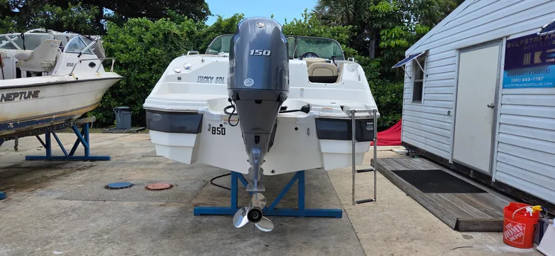 Slide: The Image of 2019 NauticStar 223DC Sport Deck boat on stand, with Yamaha 150 engine, near a white building. - 4