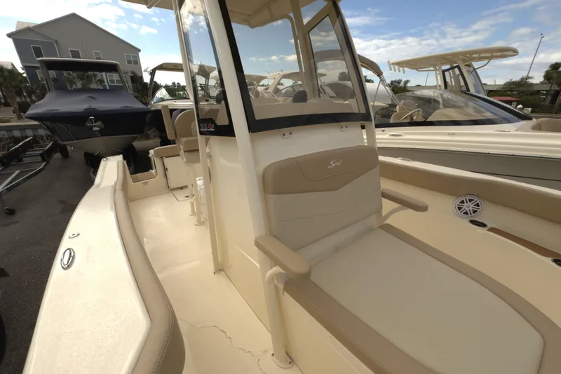 Slide: The Image of 2025 Scout 215 XSF boat interior with beige seating and console, docked outdoors. - 7