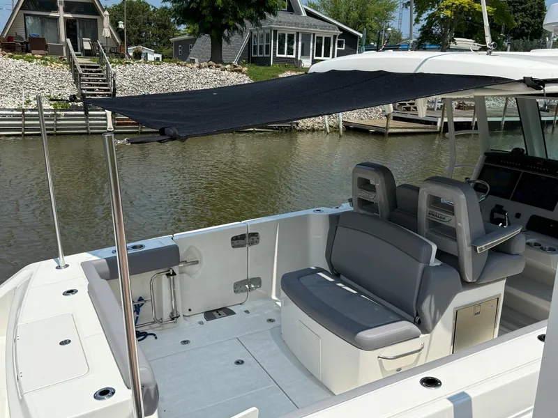 Slide: The Image of 2024 Boston Whaler 330 Outrage boat interior with seating and canopy, docked by waterfront homes. - 11