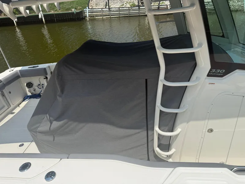 Slide: The Image of 2024 Boston Whaler 330 Outrage boat with covered seating area and ladder, docked by water. - 23