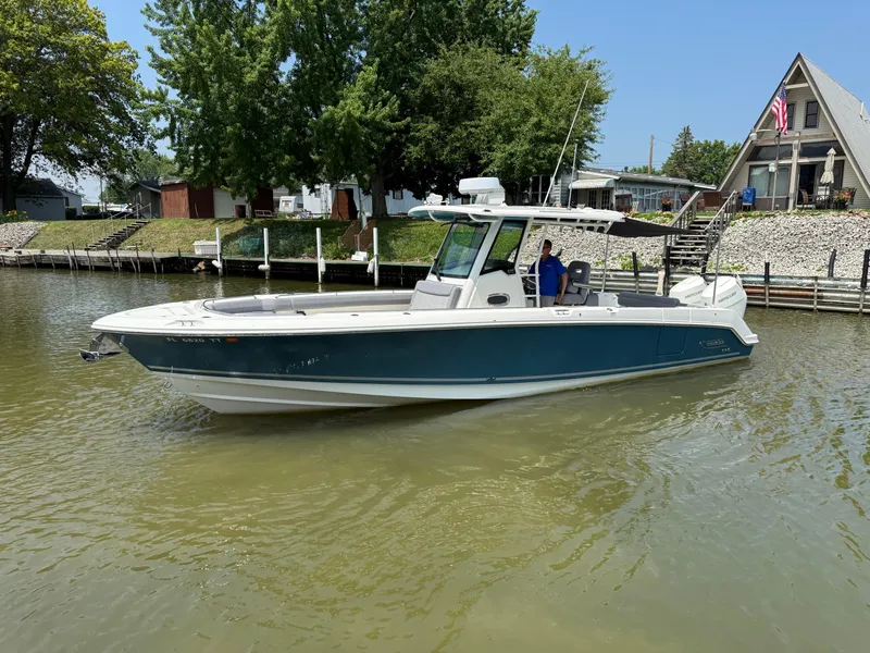 Slide: The Image of 2024 Boston Whaler 330 Outrage boat on calm water near a dockside house. - 5