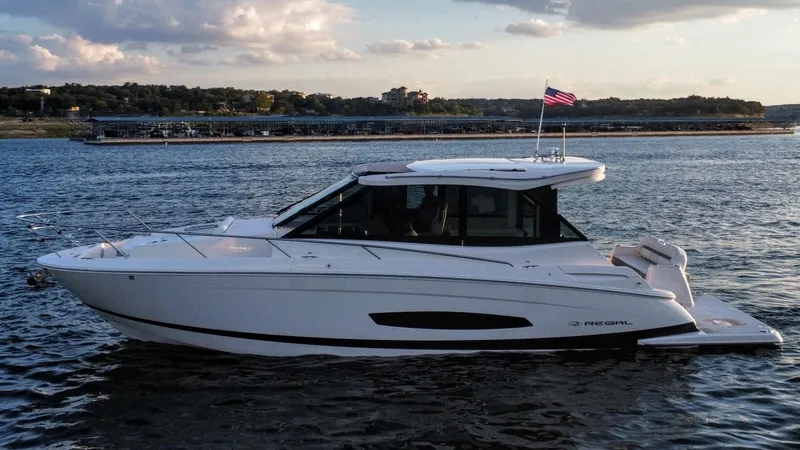 Slide: The Image of 2021 Regal 36 Grande Coupe yacht cruising on a serene lake at sunset. - 10