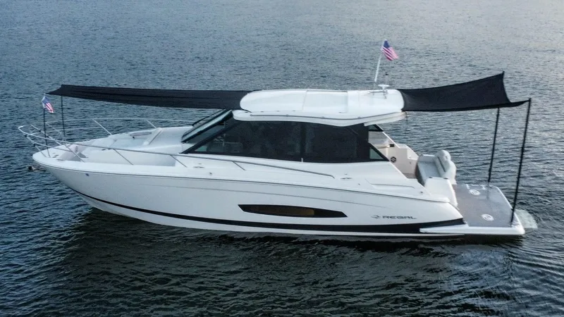 Slide: The Image of 2021 Regal 36 Grande Coupe yacht on water with sunshade and flags. - 11
