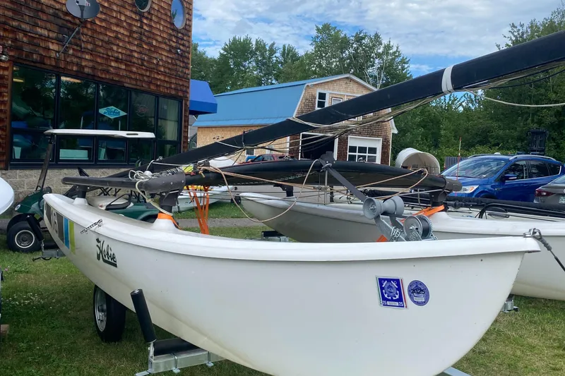 Slide: The Image of 2017 Hobie 16 catamaran on trailer, parked near rustic building and vehicles. - 2