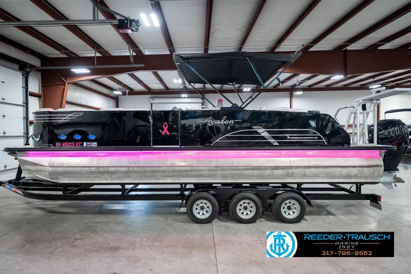 Slide: The Image of 2019 Avalon Ambassador 27' pontoon boat with pink lighting, displayed indoors on a trailer. - 11